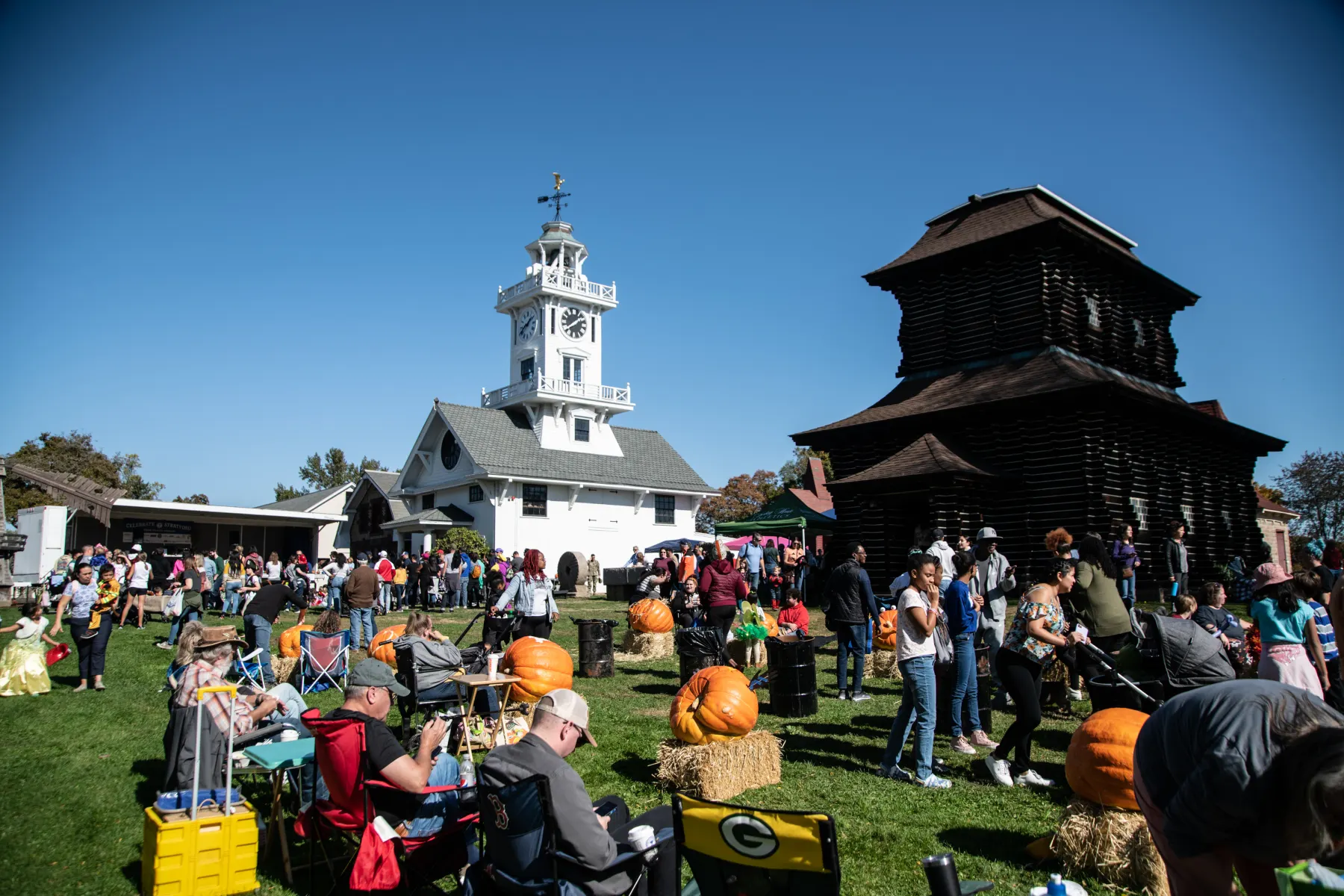 Families gathered near pumpkins and historic buildings during the Great Pumpkin Festival at Boothe Park