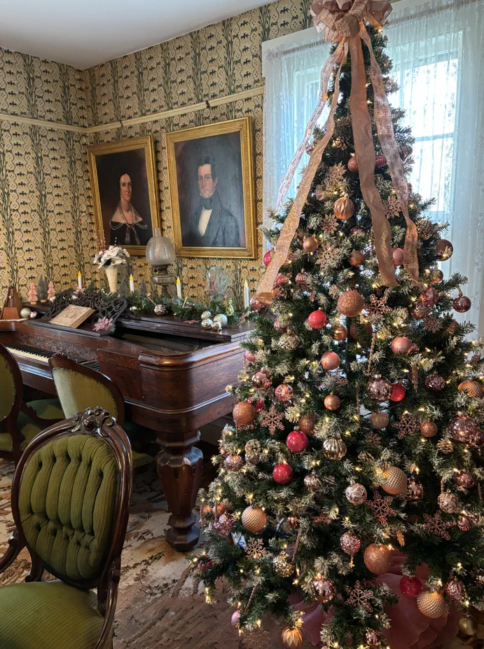 Christmas tree beside the piano and family portraits in the Boothe Homestead